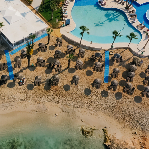 overhead view of resort on beach. several beach chairs and umbrellas on sandy beach near private ppol
