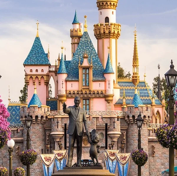 Blue and pink disneyland castle and partners statue featuring Walt Disney holding hands with Mickey Mouse at dusk
