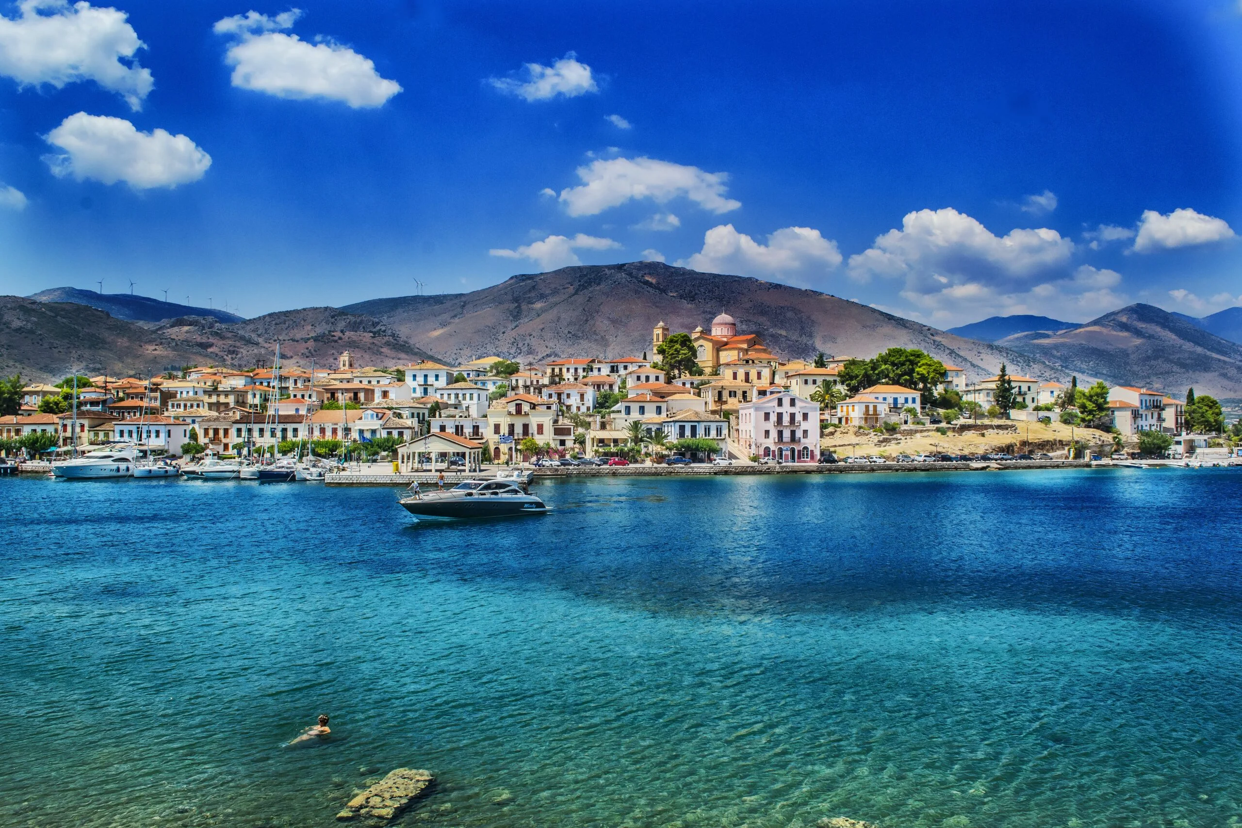Mediterranean coast. colorful historic buildings and a small boat near shore. dark blue water, mountains in background