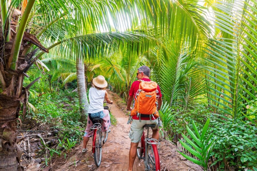a couple rides bikes down a jungle trail on an excursion during virgin voyages cruises